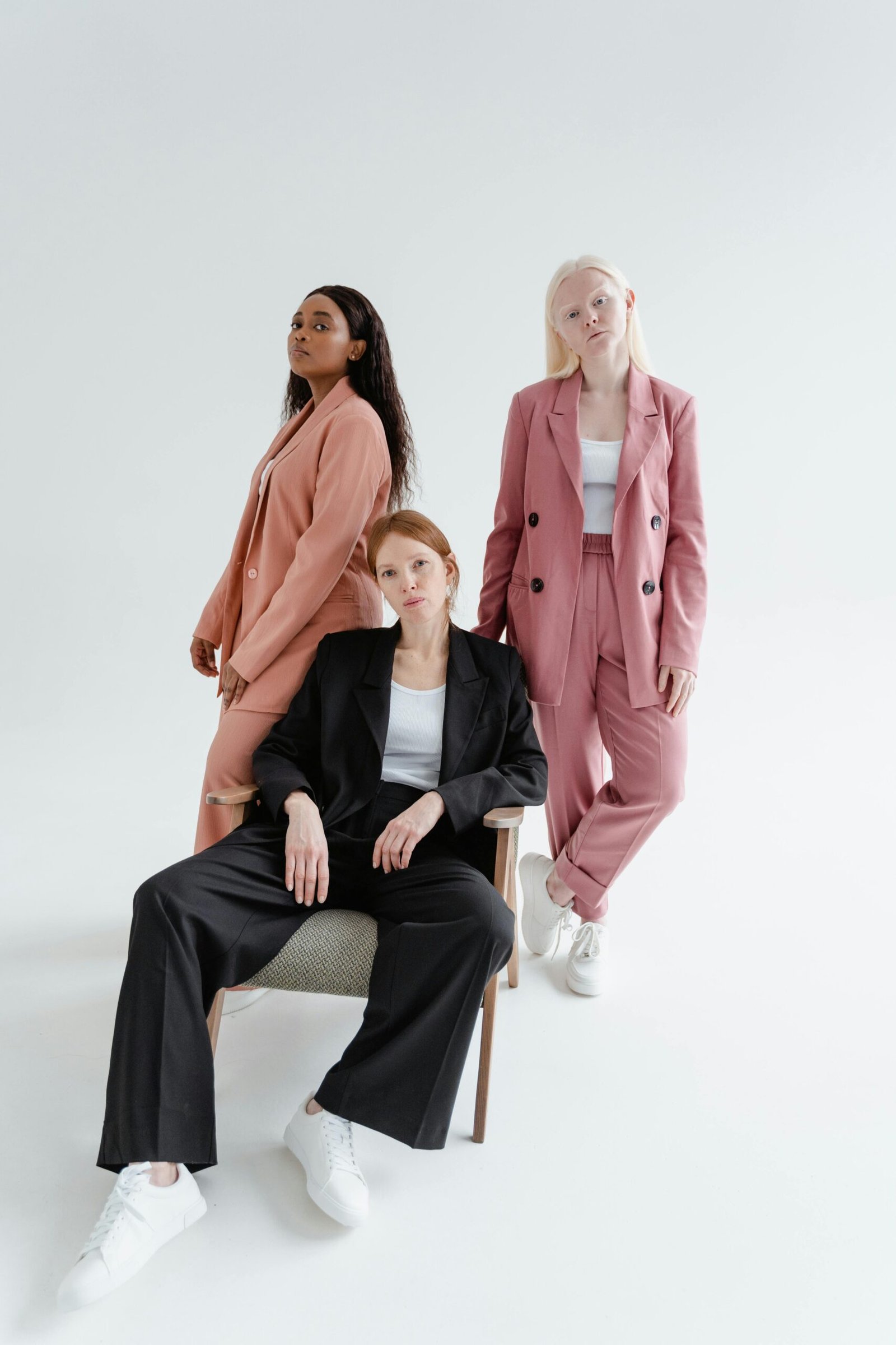 Three stylish women in blazers posing confidently in a bright studio setting.